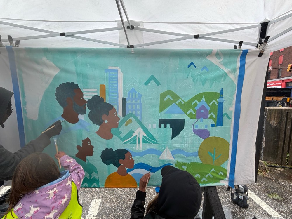 Volunteers painting a large Baltimore skyline mural on canvas beneath a pop-up tent